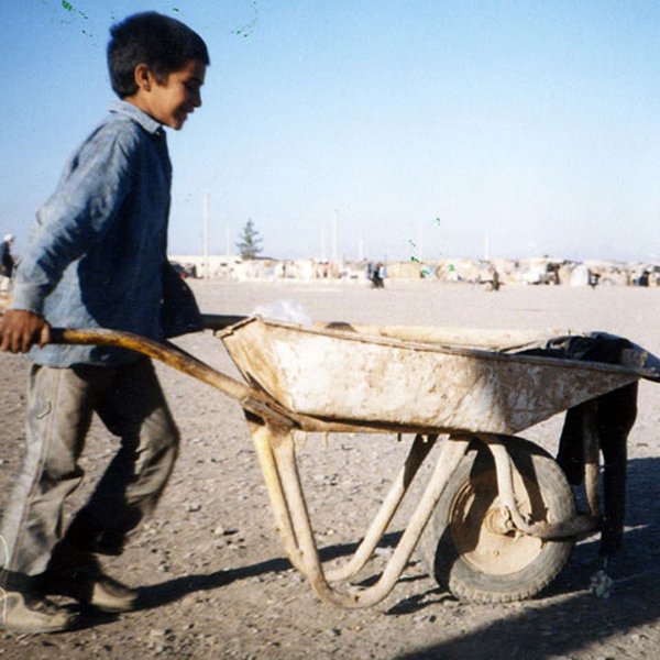 Child pushing a wheelbarrow outside of refugee camp