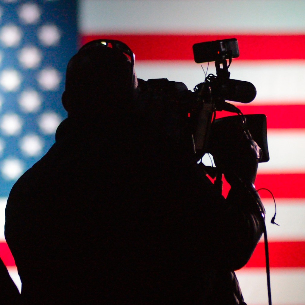 Silhouette of man holding video camera in front of the American flag
