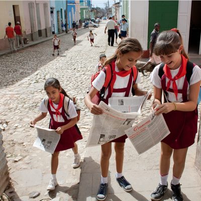 Three Cuban school girls opening up newspapers