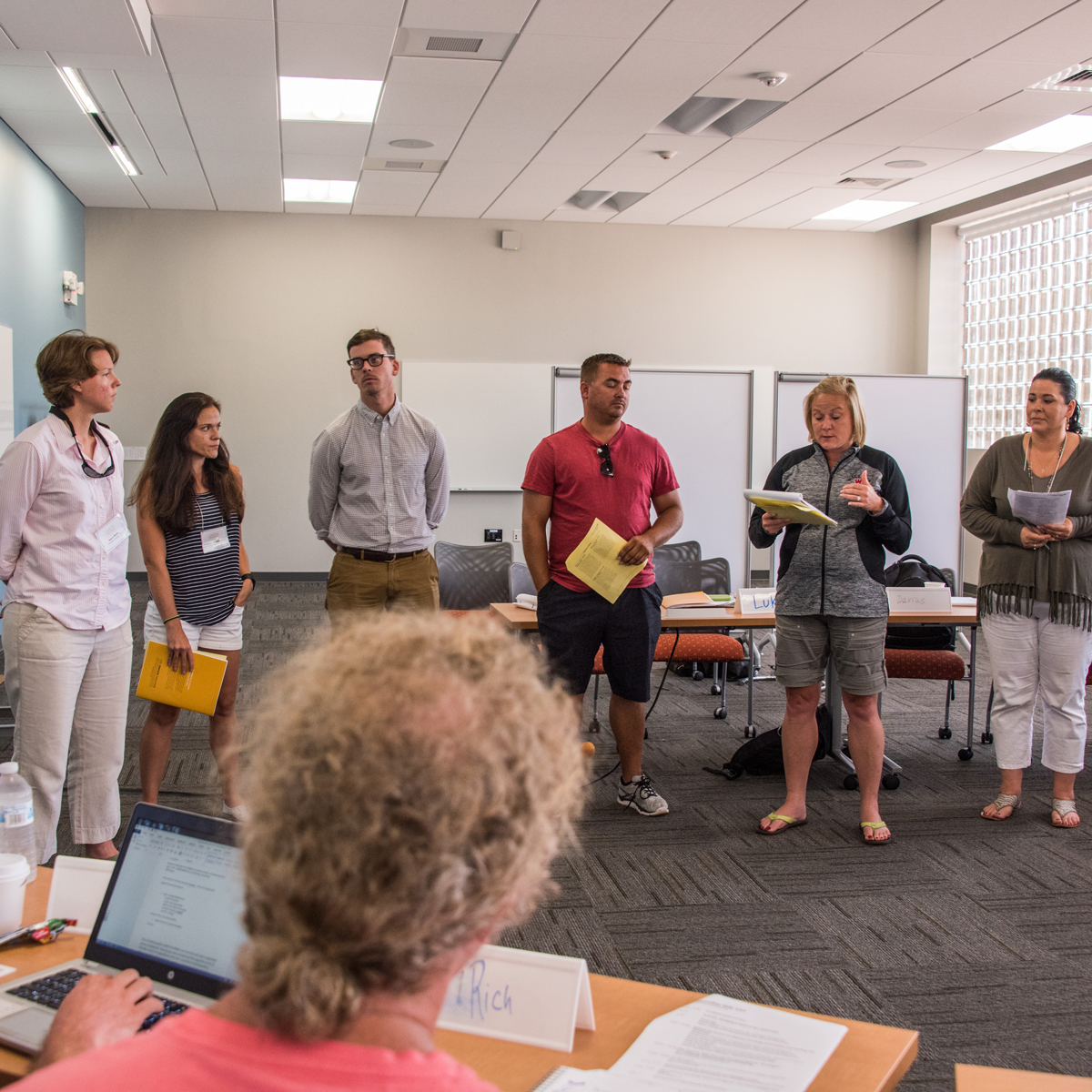 People standing in a row listening to a woman speak