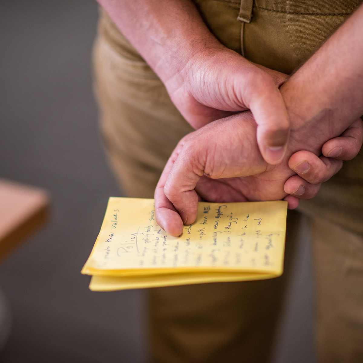 Close up of a person holding their hands behind their back holding a notepad that says Policy