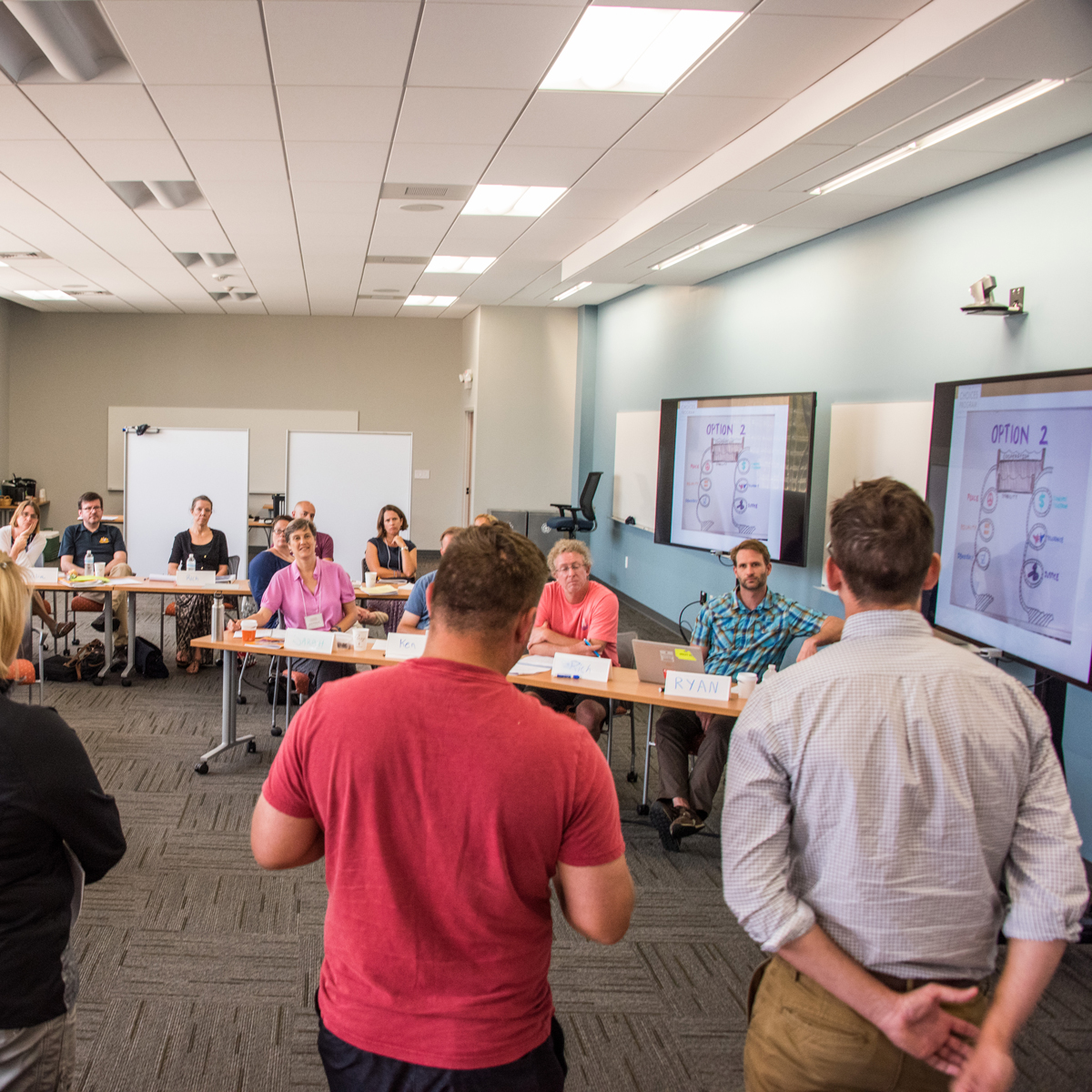 Row of people present to other adults sitting at desks