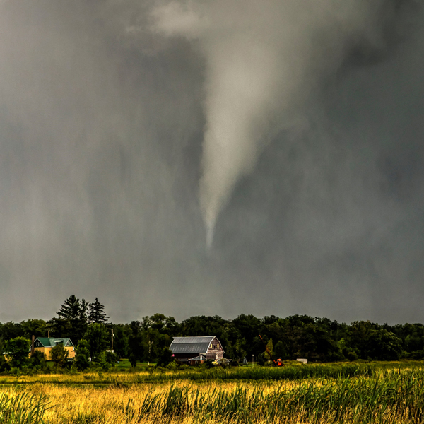 A tornado above a house on the edge of a field