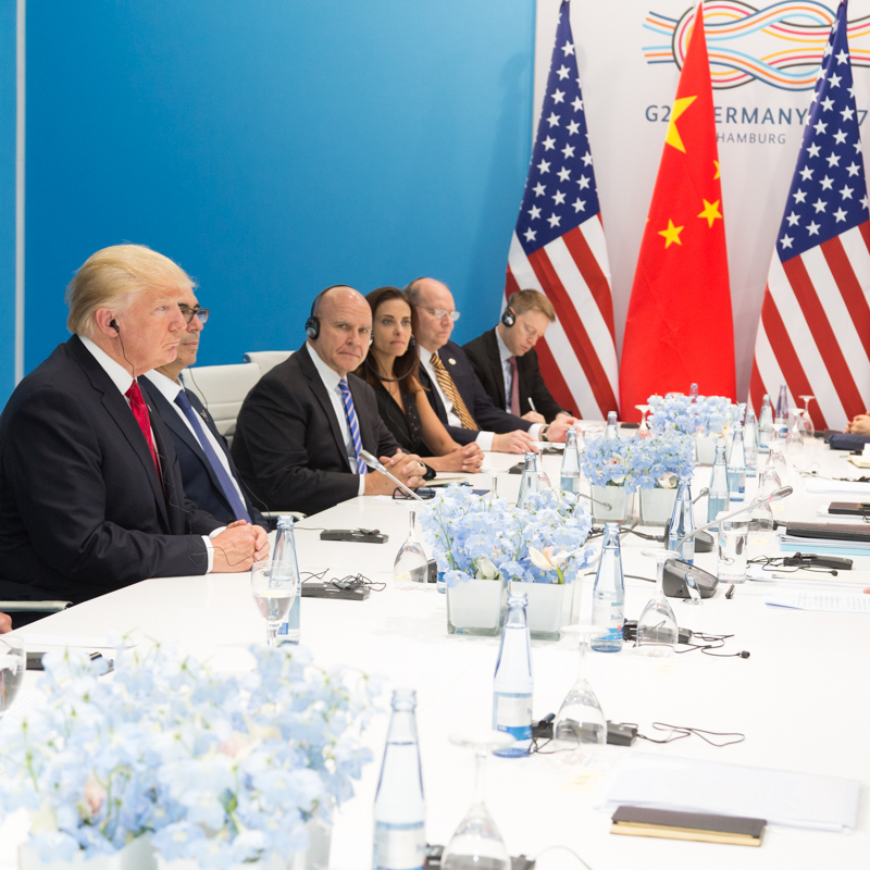 Donald Trump sitting at a table negotiating with U.S. and Chinese officials