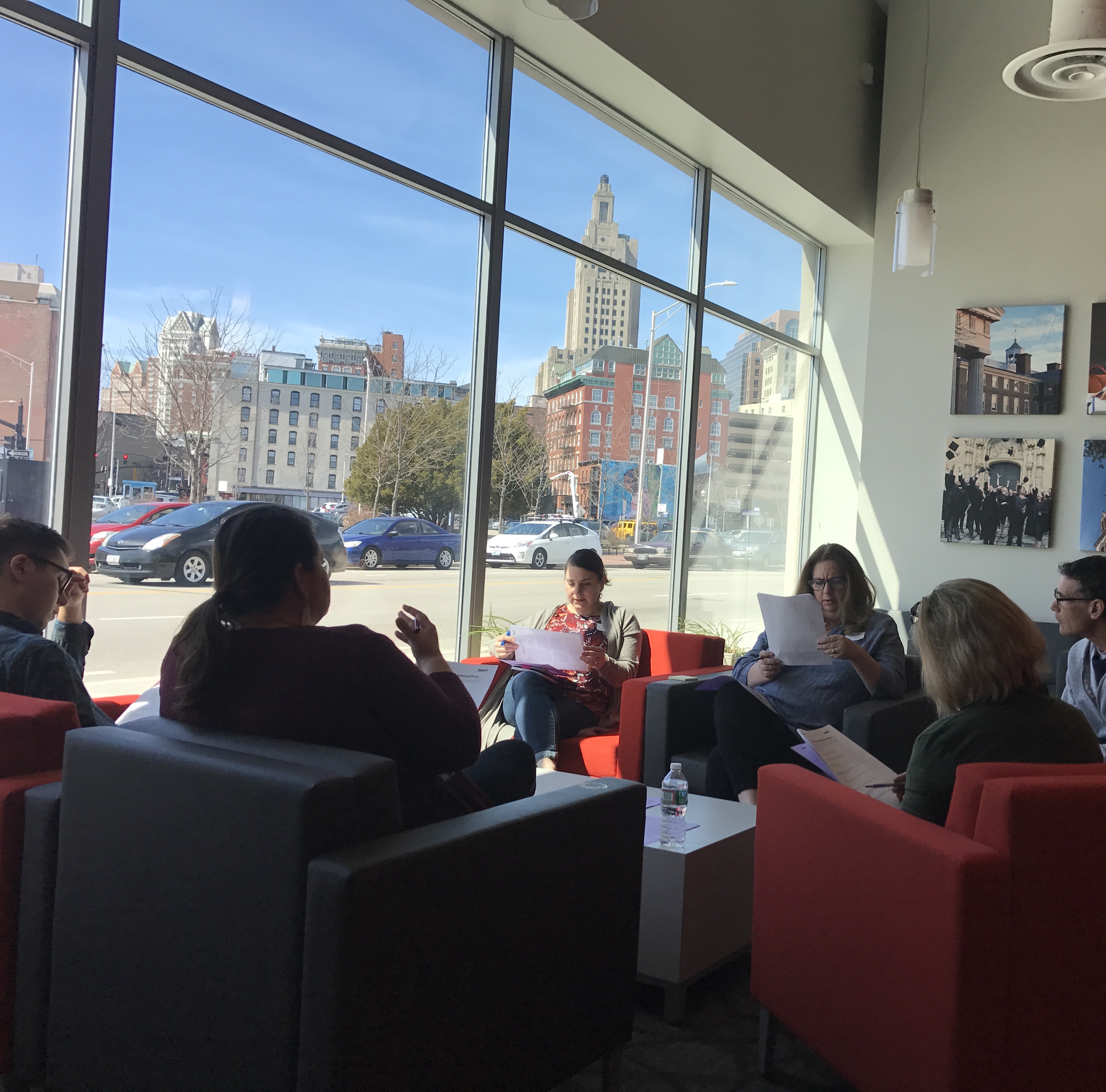 People sitting in chairs and reading papers by a window