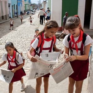 Three Cuban school girls opening up newspapers