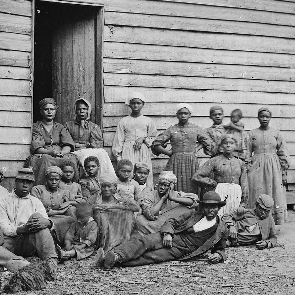 Group of fugitive slaves sitting outside a log house