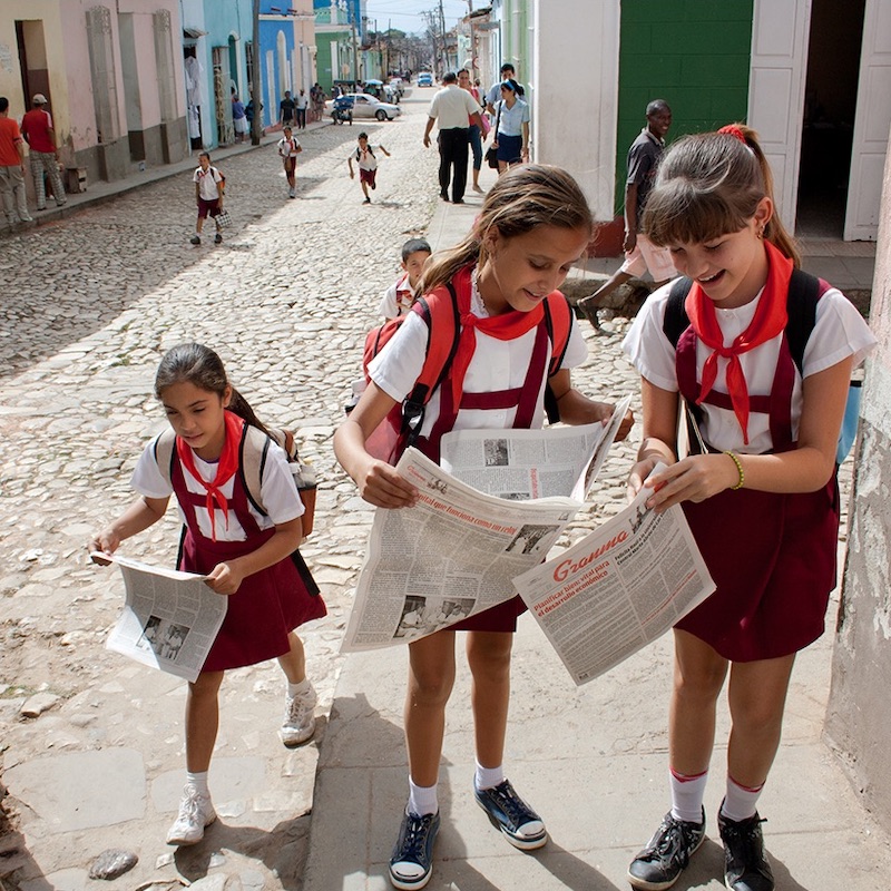 Three Cuban school girls opening up newspapers