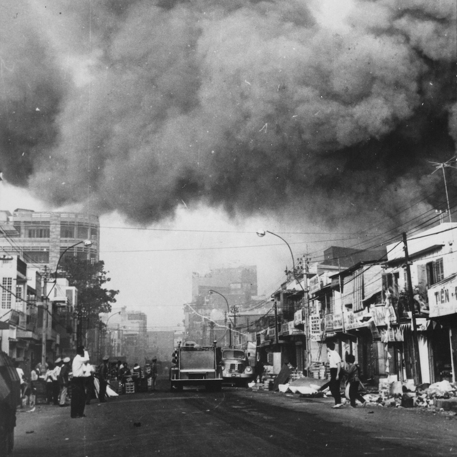 Saigon under fire during the Vietnam War, 1968. Black and white photo of a street with huge clouds of smoke billowing overhead.