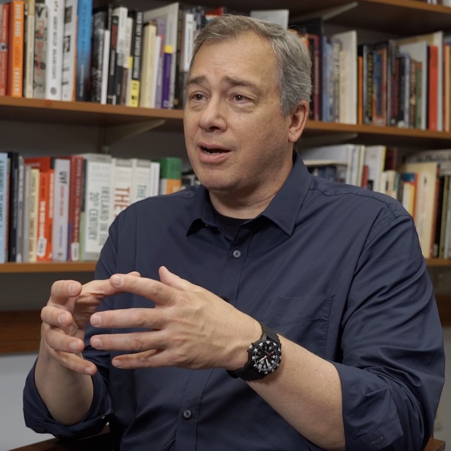 Professor James Waller sits in front of a large bookshelf filled with books as he appears in the Choices Program video series on genocide.