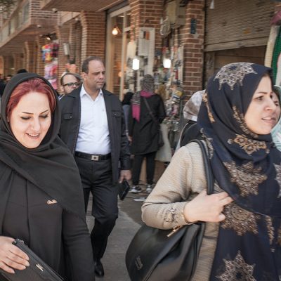 Women wearing headscarves walk along a crowded sidewalk