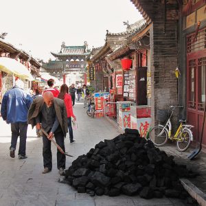 An older man shovels a small pile of coal on a pedestrian street in China.
