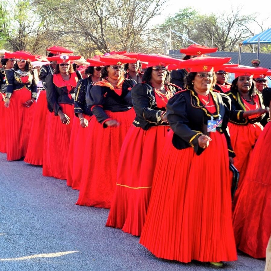 OvaHerero women who are members of a fraternity called Otjiserandu that honors their ancestors line up where their signature uniforms that include a floor-length red skirt, black jacket, and unique red hats made to resemble cow horns.