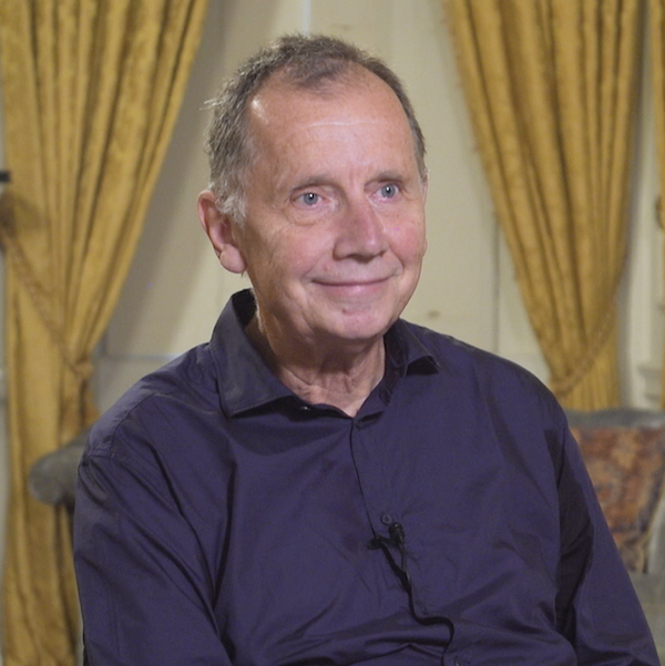 Photo of Dietrich Neumann as he appears in the Choices Program's video series. He is seated in front of gold-colored curtains.